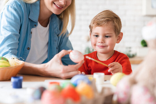 Close up portrait of cheerful happy mother and little son decorating Easter eggs at home. Togetherness and family time concept. Mom and small kid child painting for holiday
