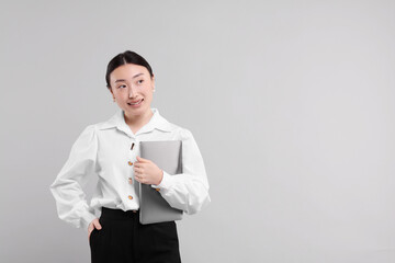 Portrait of smiling businesswoman with laptop on grey background. Space for text