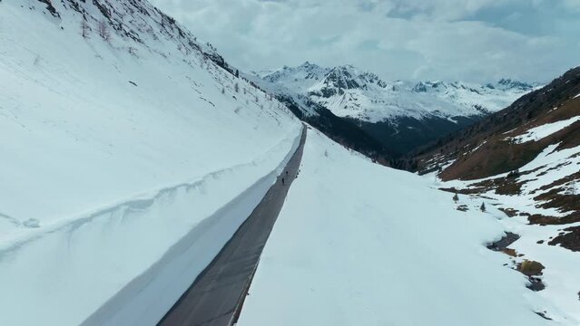 Two professional road cyclists ride on empty secluded mountain pass in Alps. Inspiring content from cycling influencers during trip and travel in harsh conditions. Cycling in winter or early spring