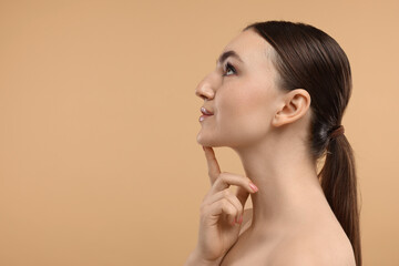 Beautiful woman touching her chin on beige background. Space for text