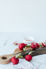 chopped radishes lie on a wooden cutting board, next to a kitchen towel and whole radishes on a marble background