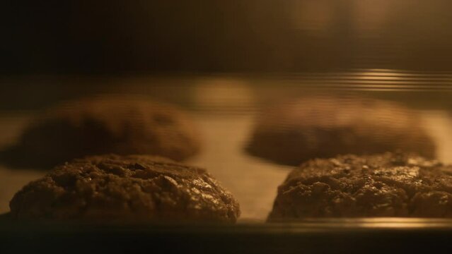 A tray of cookies is baking in an oven. The cookies are brown and appear to be chocolate chip. baking cookies in a hot oven and many pieces. Making bakery desserts.