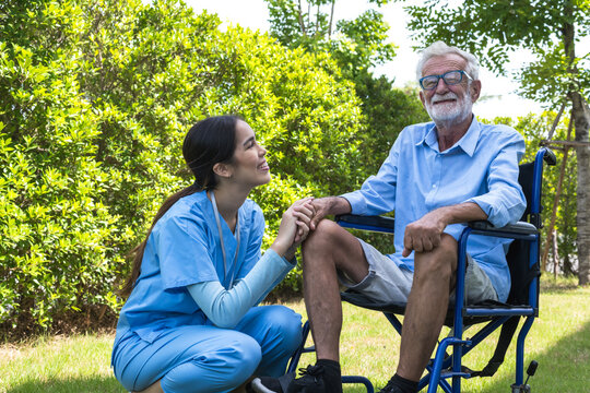 Friendly Asian care taker take care of elderly Caucasian retirement man sitting on wheelchair in home care garden