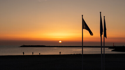People on beach watching sunset over North Sea and South Pier of Hvide Sande harbor, Mid Jutland, Denmark