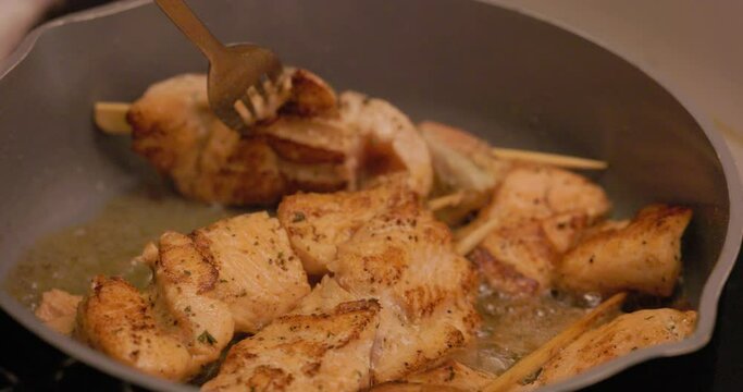 The footage captures the tantalizing process of cooking skewered chicken pieces as they sizzle in a saute pan, seasoned to perfection and turned for an even golden-brown sear. The steam and spices