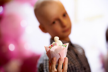 A boy holds a cupcake with mastic in a package in his hand