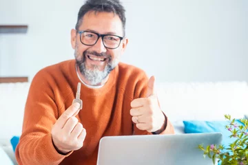 Fotobehang One cheerful adult man showing new hone ket and thumb up smiling at the camera. Finding house apartment online on website concept. Searching property on web. Business real estate people and notebook © simona