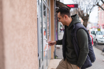 A one young man withdrawing money on ATM with credit card in the city