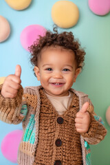 Fototapeta na wymiar Cheerful toddler giving thumbs up with copy space on pastel background