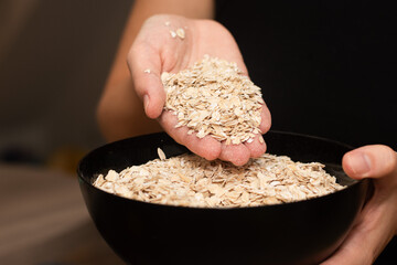Oats Trickling from Hand into Bowl. Hand sprinkling rolled oats into a black bowl.