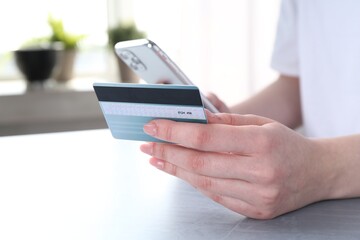 Online payment. Woman with smartphone and credit card at white table, closeup