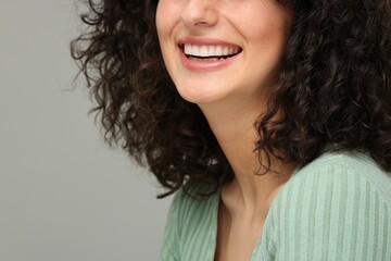 Young woman using teeth whitening strip on grey background, closeup. Space for text