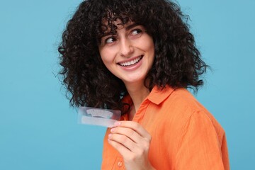 Young woman holding teeth whitening strips on light blue background
