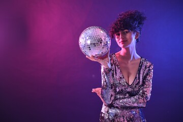 Naklejka premium Beautiful young woman with disco ball posing on color background in neon lights. Space for text