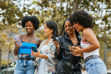 Diverse women and transgender person using phone together outdoors