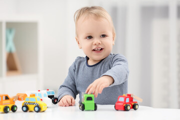 Children toys. Cute little boy playing with toy cars at white table in room