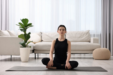 Beautiful girl meditating on yoga mat at home
