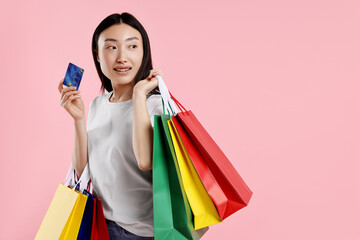 Smiling woman with shopping bags and credit card on pink background. Space for text