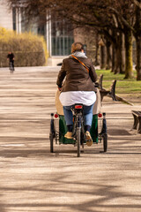 A mother transports her children in a cargo bike through a park.