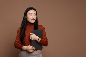 Fototapeta premium Portrait of smiling woman with laptop on brown background. Space for text