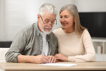 Senior couple signing Last Will and Testament indoors