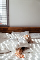 Litttle child sleeping in bed hugging teddy bear with his feet sticking out from under the blanket at sunny morning. Focus on feet. Copy space