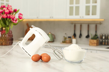Modern mixer, eggs and bowl with flour on white marble table in kitchen