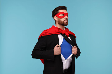 Obraz na płótnie Canvas Confident businessman wearing superhero costume under suit on light blue background