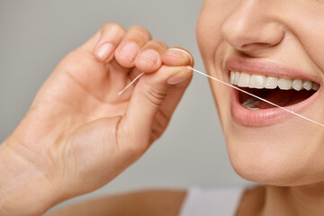 excited cropped woman holding dental floss and smiling on grey background,  promoting oral hygiene