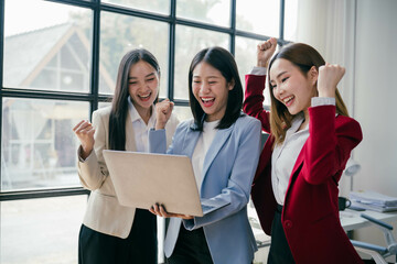 Three women are smiling and celebrating in front of a laptop