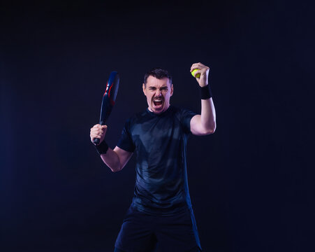 Padel tennis tour player in white sportswear. Man athlete with paddle tenis racket on black background celebrating a set win. Sport concept. Download a high quality photo for sports website.