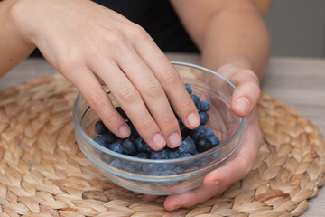 Fresh Blueberries in a Glass Bowl in Female Hands. Picking ripe blueberries from a glass bowl.