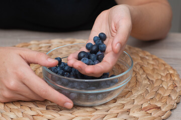 Fresh Blueberries in a Glass Bowl in Female Hands. Picking ripe blueberries from a glass bowl.