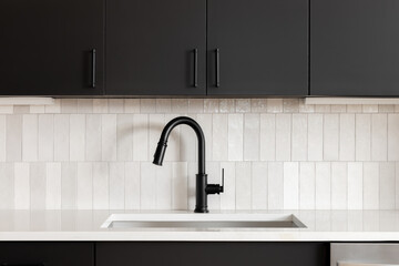 A kitchen faucet detail with black cabinets, a vertical subway tile backsplash, and a black faucet...