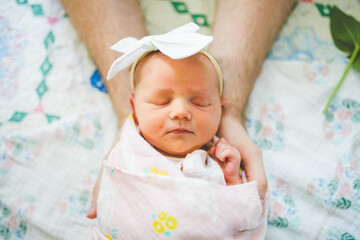 Beautiful Newborn Girl Photo of Baby Girl Swaddled in Pink Blanket Held in Dad's Hands, Vintage Quilt, Baby Swaddle, and Flower Stem in Background