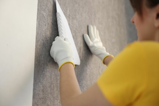 Woman smoothing stylish gray wallpaper in room, closeup
