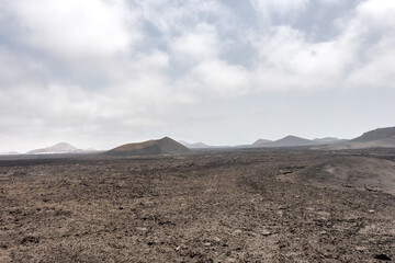 A deserted volcanic scenery with a vast lava field and multiple small volcano craters on the background, Timanfaya National park, Lanzarote, Canary islands