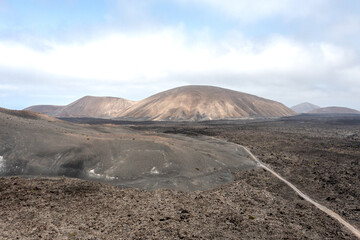 A road going through lava fields towards multiple small volcanoes in Timanfaya National park, Lanzarote, Canary islands