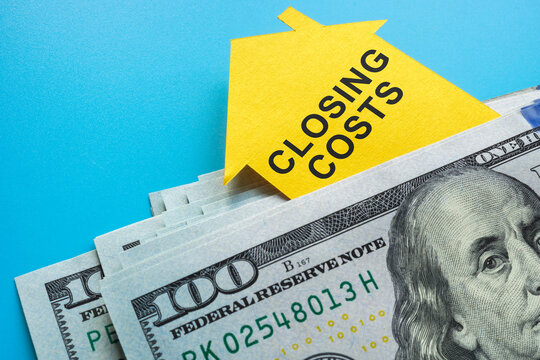 A stack of money and a paper house with an inscription closing costs.