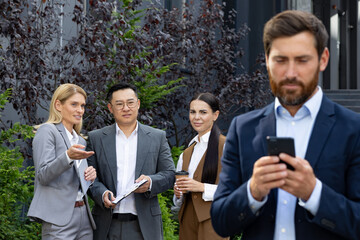 Diverse group of colleagues standing behind man with cell phone in hands and having discussion with...