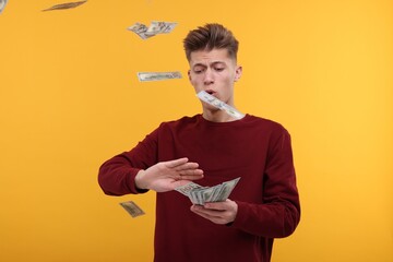 Handsome man throwing dollar banknotes on yellow background