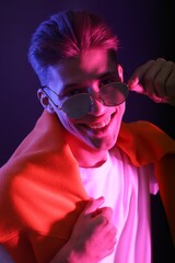 Stylish young man in sunglasses on dark background in neon lights