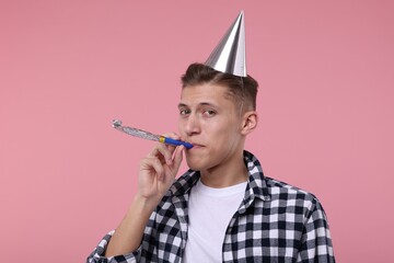 Young man in party hat with blower on pink background