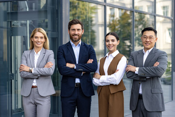 Four confident employees wearing business clothes and smiling widely to camera with arms folded on...