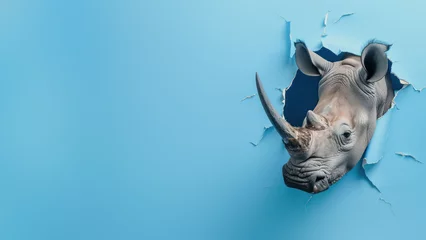 Zelfklevend Fotobehang A powerful image of a rhinoceros breaking through a bright blue paper wall, symbolizing breakthrough and strength © Fxquadro