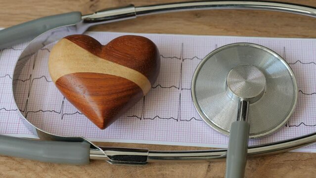 Placing wooden hearth next to electrocardiogram and medical stethoscope. Cardiology or heart health concept