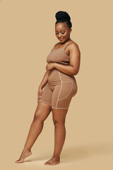 Curvy smiling Black woman wearing high waisted shaper shorts and sports bra - obrazy, fototapety, plakaty