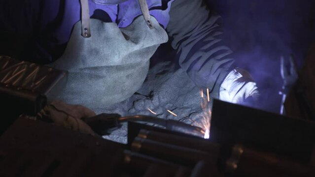An employee in protective equipment works with a professional welding machine at one of the stages of manufacturing a metal part at a production or metallurgical plant