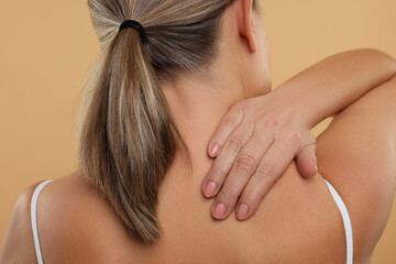 Mature woman suffering from pain in her neck on beige background, back view