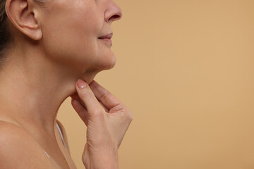 Fototapeta premium Mature woman touching her neck on beige background, closeup. Space for text